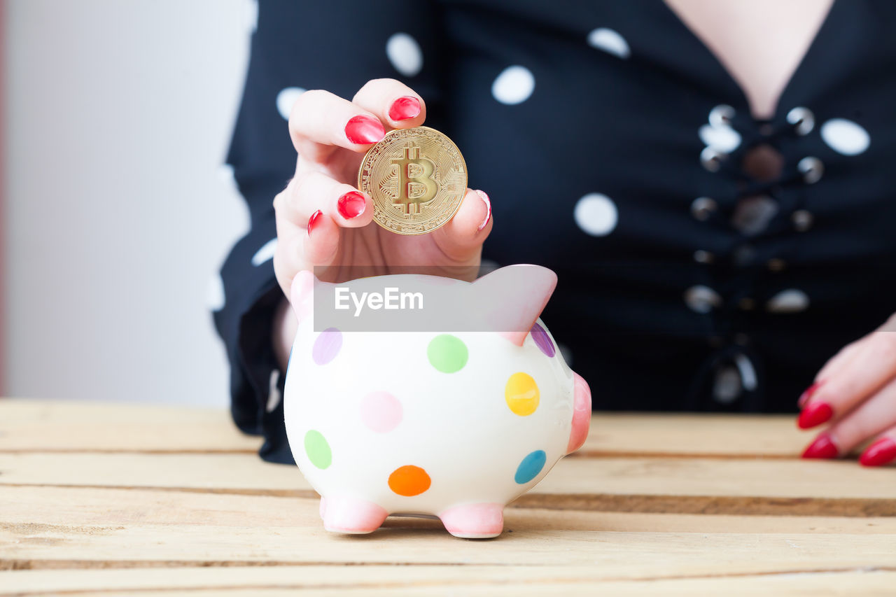 Midsection of woman putting coin in piggy bank on table