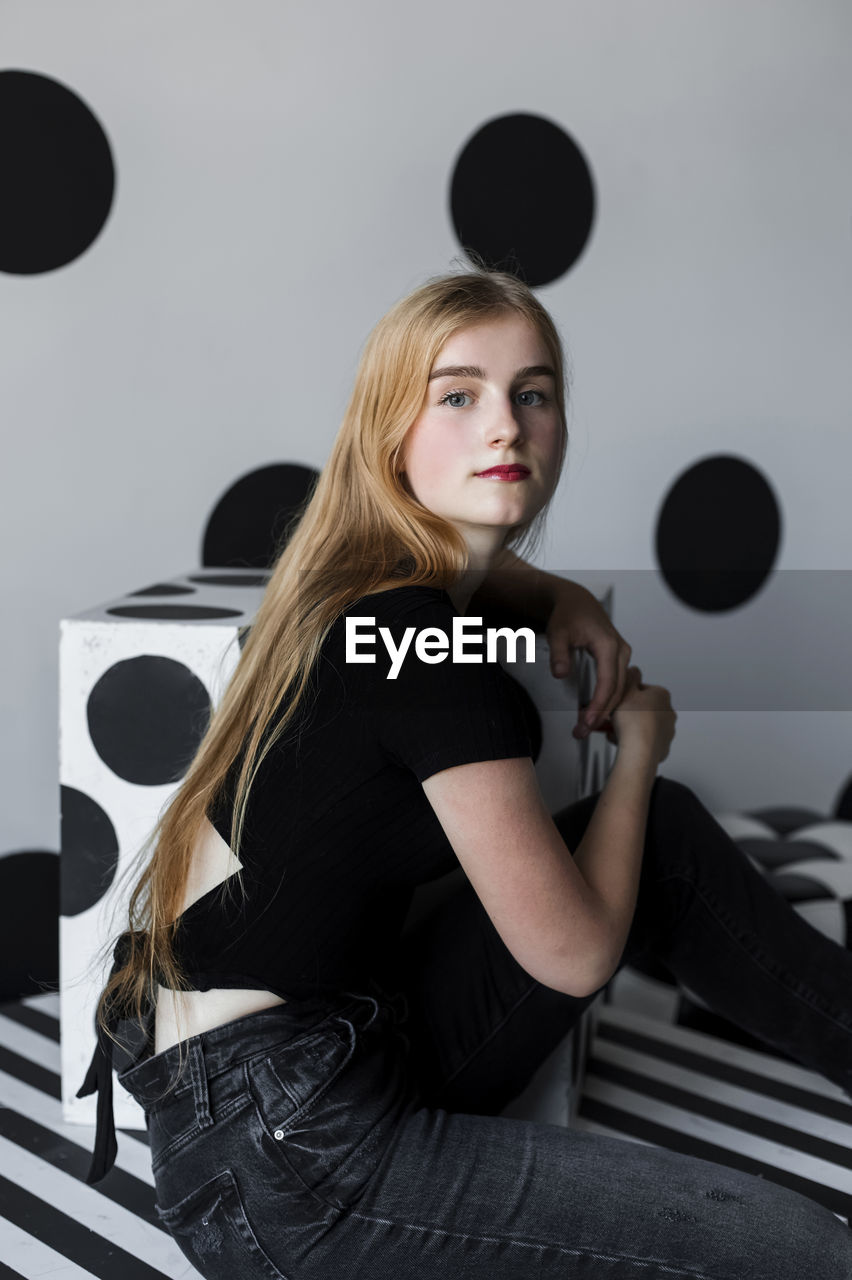 Beautiful teenage girl sitting in front of dotted wall