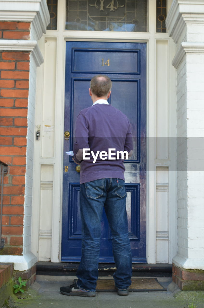 REAR VIEW OF MAN STANDING OUTSIDE HOUSE