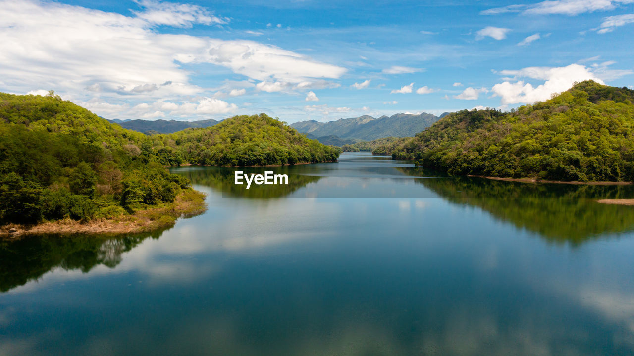 A river among mountains and hills with a reflecting blue sky and clouds. randenigala reservoir