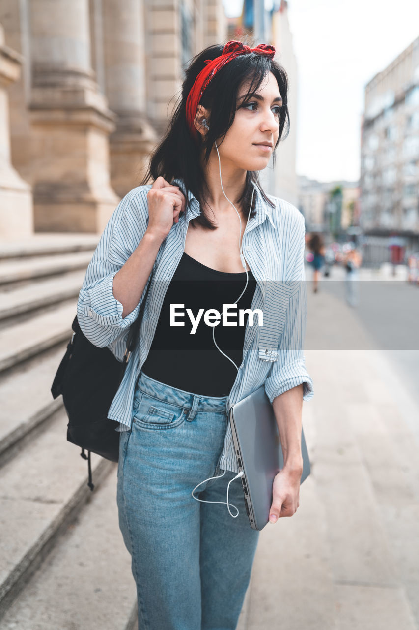 Young woman holding laptop standing in city