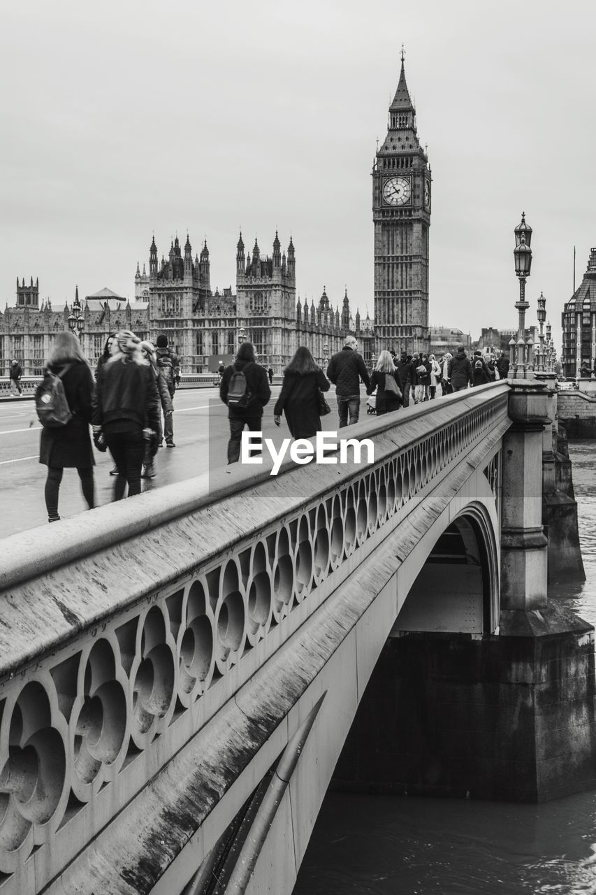 People walking on westminster bridge by big ben against sky in city