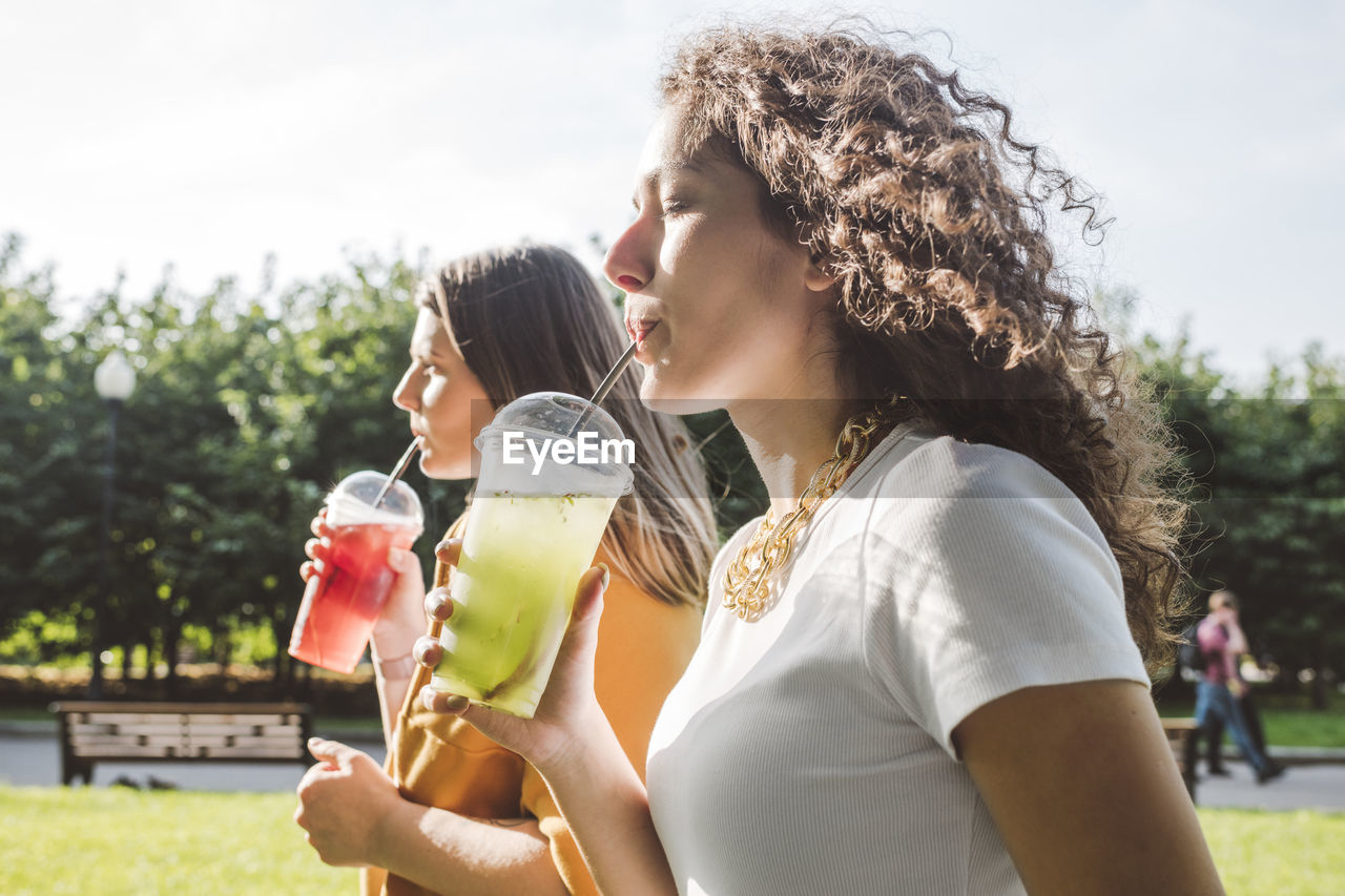 Female friends drinking fresh lemonades while walking at park on sunny day