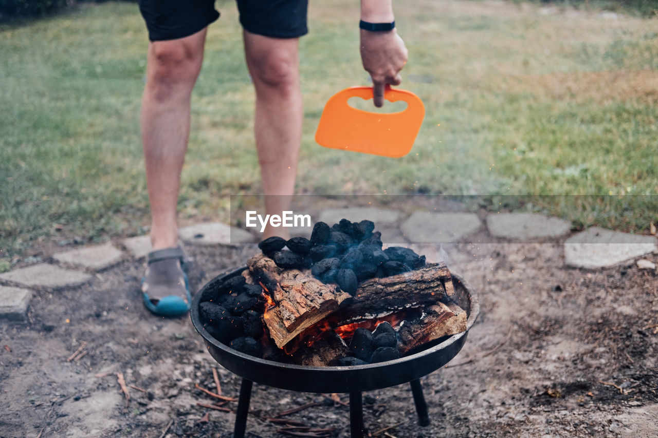 How to use a charcoal grill. man with plastic bbq hand fan near charcoal grill fire. barbeque