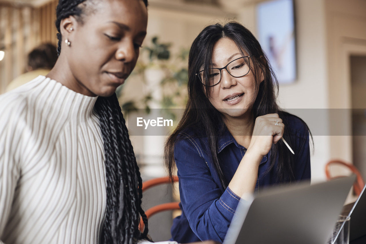 Businesswoman discussing with female colleague over laptop at coworking office