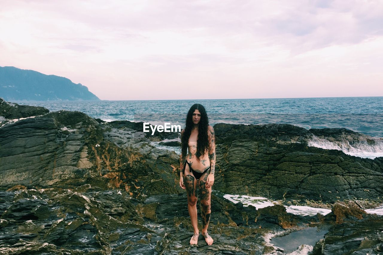 Woman standing on rock by sea against sky