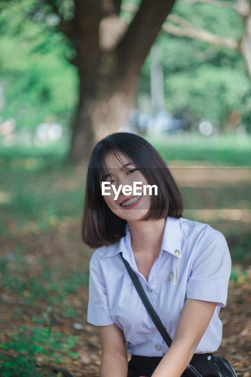 Portrait of smiling young woman sitting at park