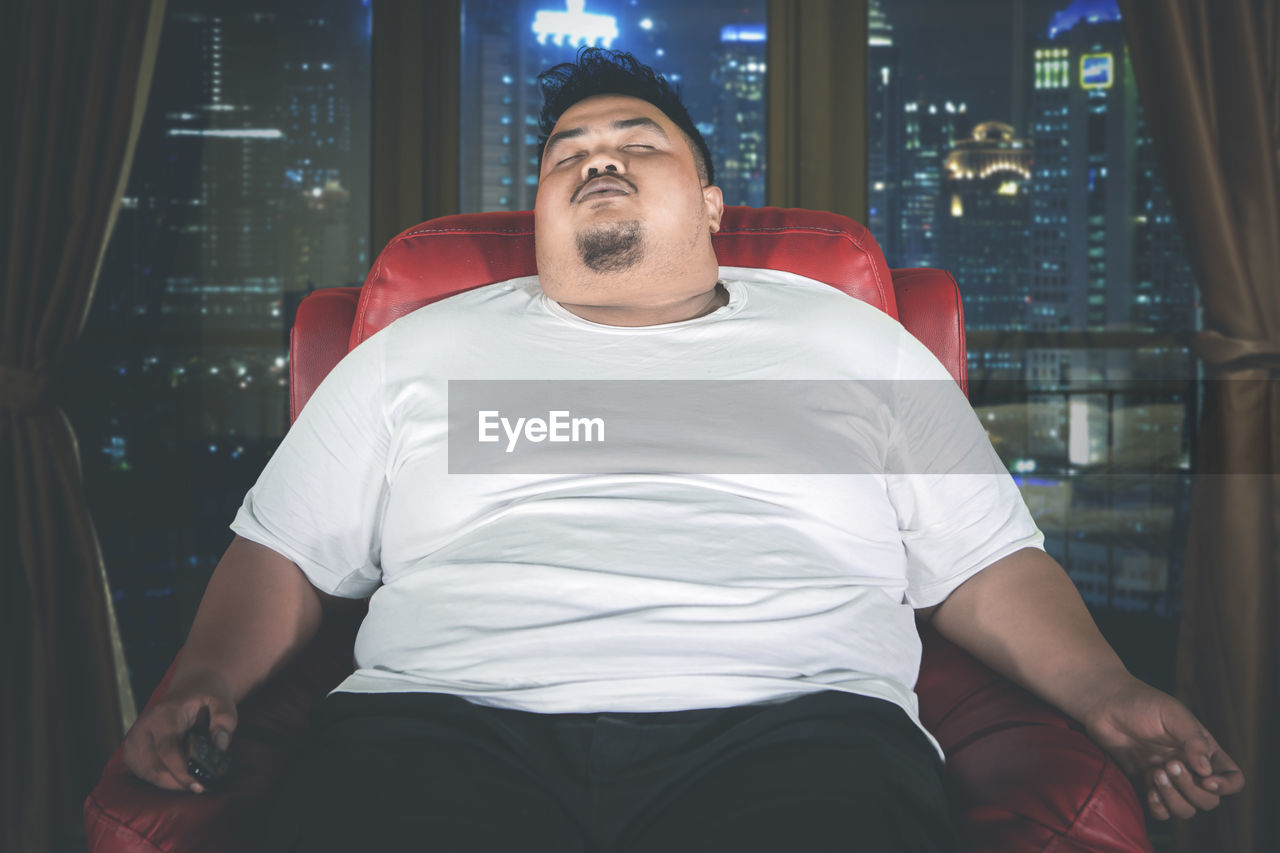 Lazy overweight young man sleeping on sofa at home during night