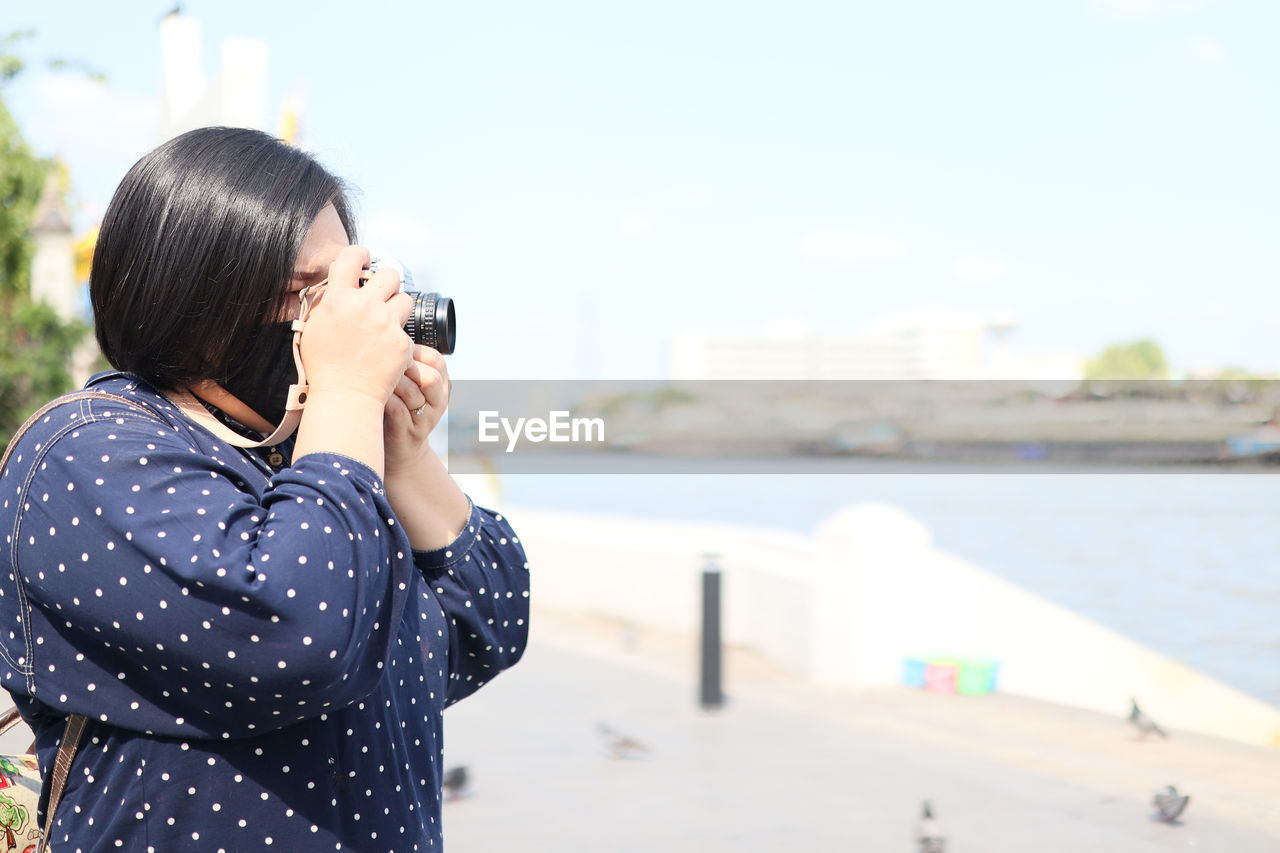 Woman wearing mask with camera standing at harbor