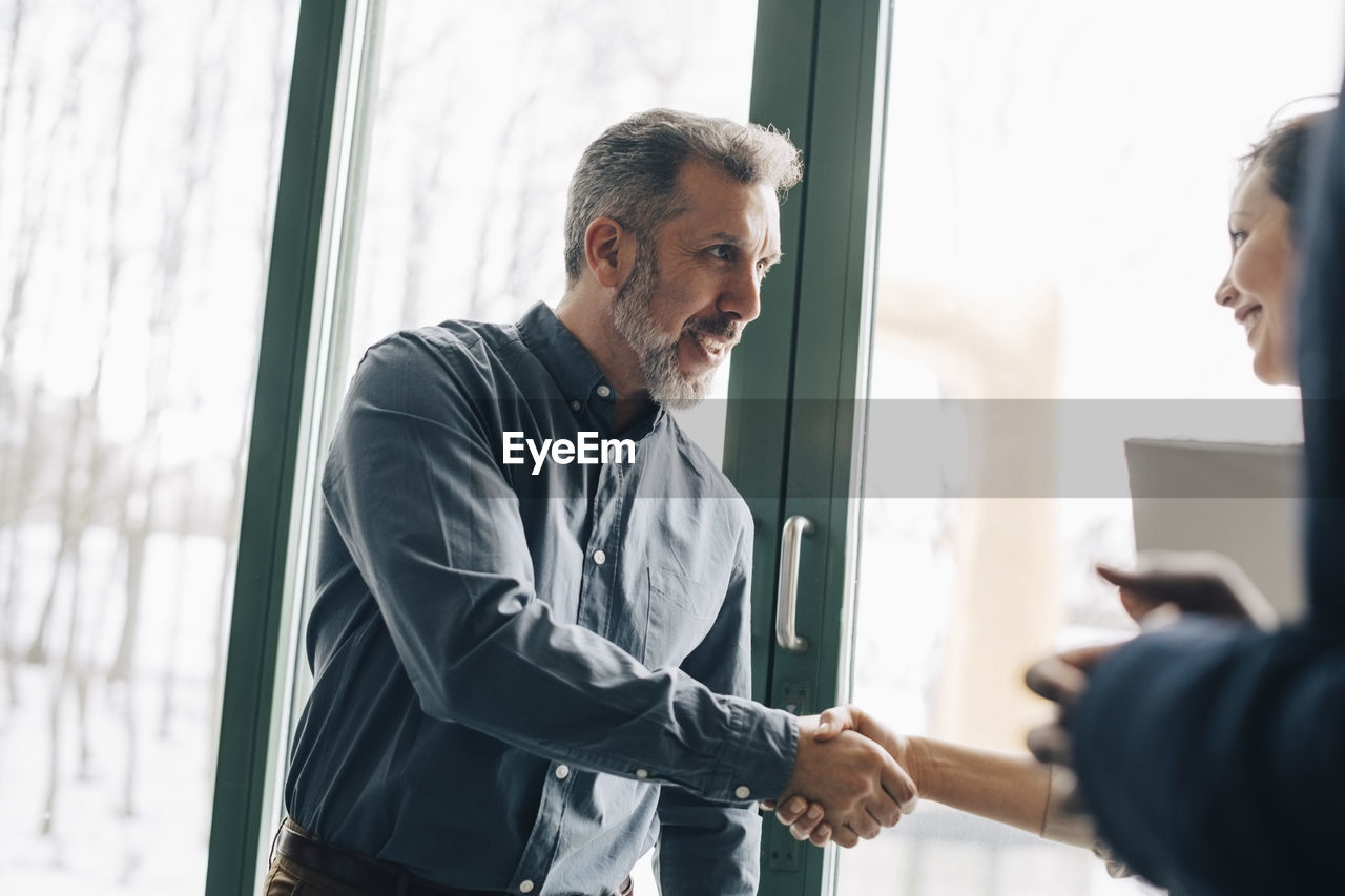 Mature businessman greeting female coworker in meeting at office