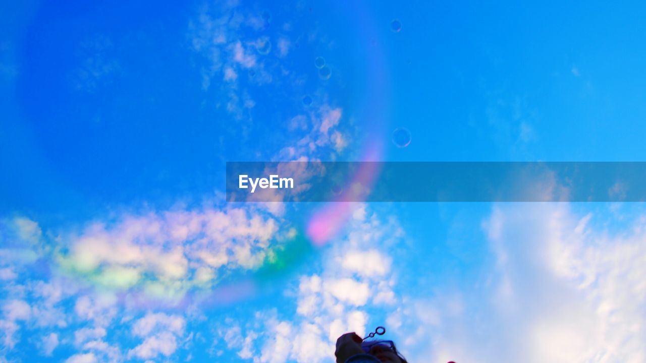 LOW ANGLE VIEW OF WOMAN STANDING AGAINST BLUE SKY