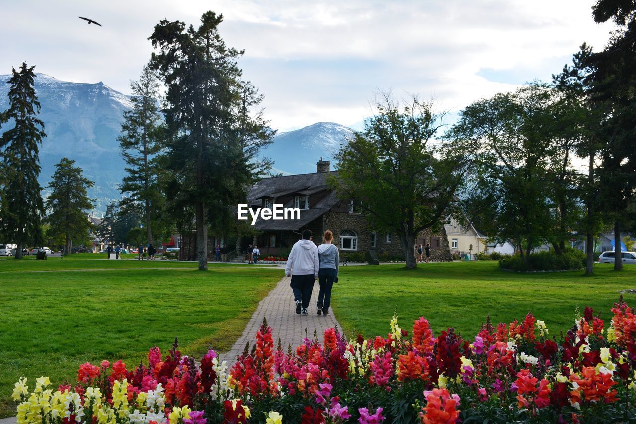 Rear view of man and woman walking on footpath in park against sky