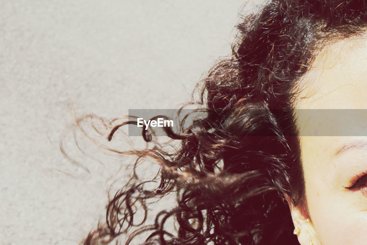 Cropped image of woman with curly hair against wall