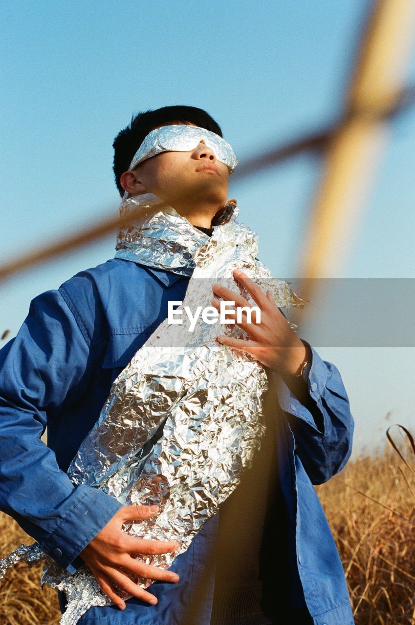 Low angle view of man with aluminum foil standing on field against sky