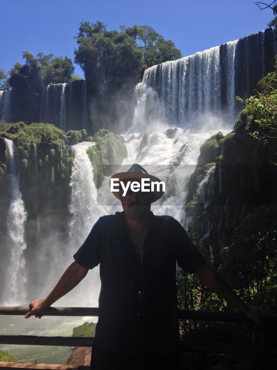 Portrait of man standing against waterfall in forest