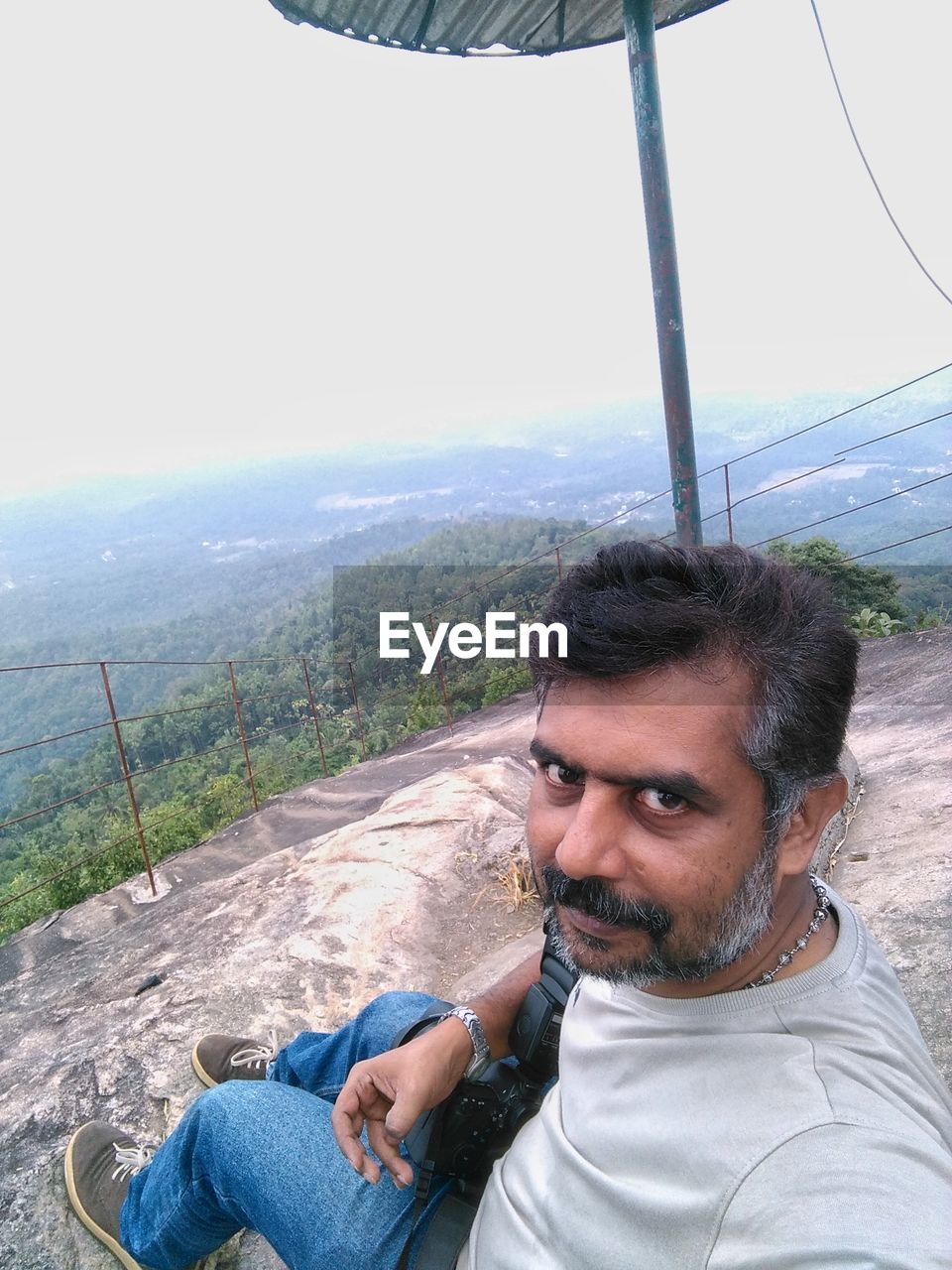 Portrait of man sitting on rocky mountain against landscape