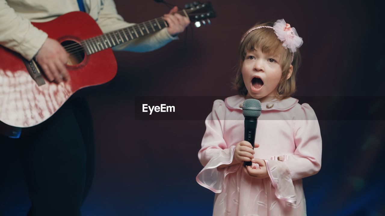 child, childhood, music, musical instrument, performance, two people, musician, men, arts culture and entertainment, indoors, guitar, singing, mouth open, string instrument, emotion, person, musical equipment, female, family, waist up, holding, concert, standing, women, human mouth, fun, adult, performing arts, clothing, baby, singer, blond hair