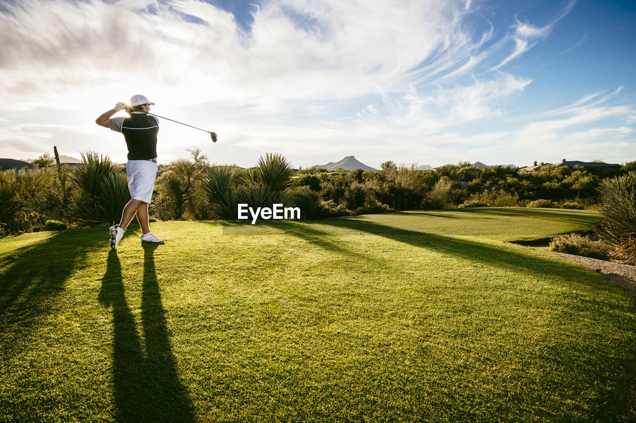 Full length of golfer playing on field against sky