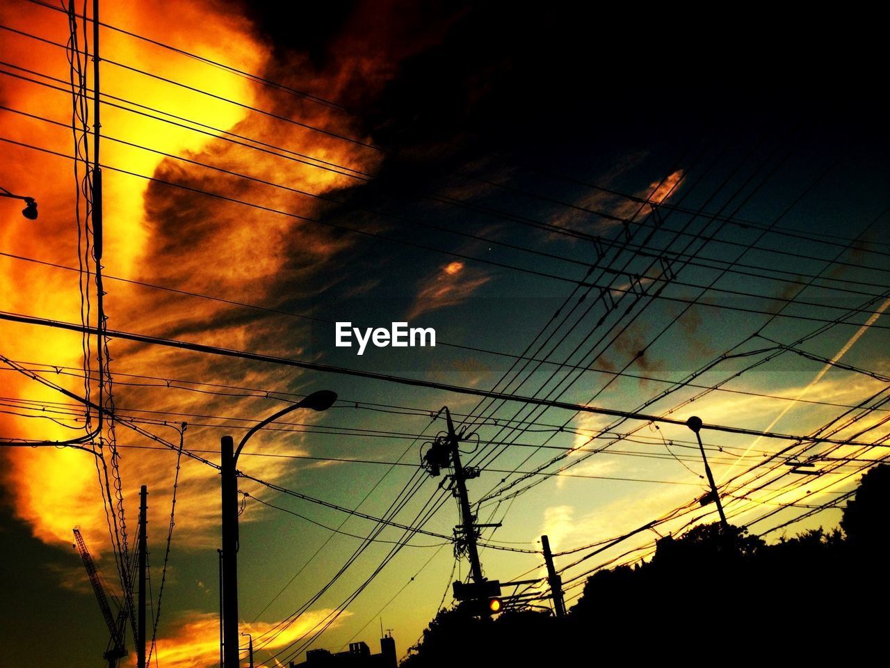 Low angle view of silhouette electricity pylons and cables against sky during sunset