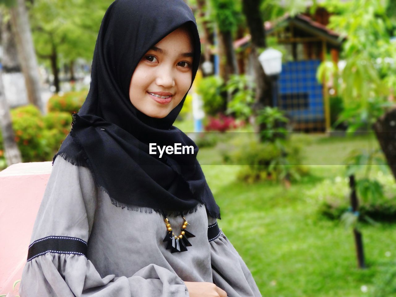 Portrait of smiling teenage girl wearing hijab while standing at back yard