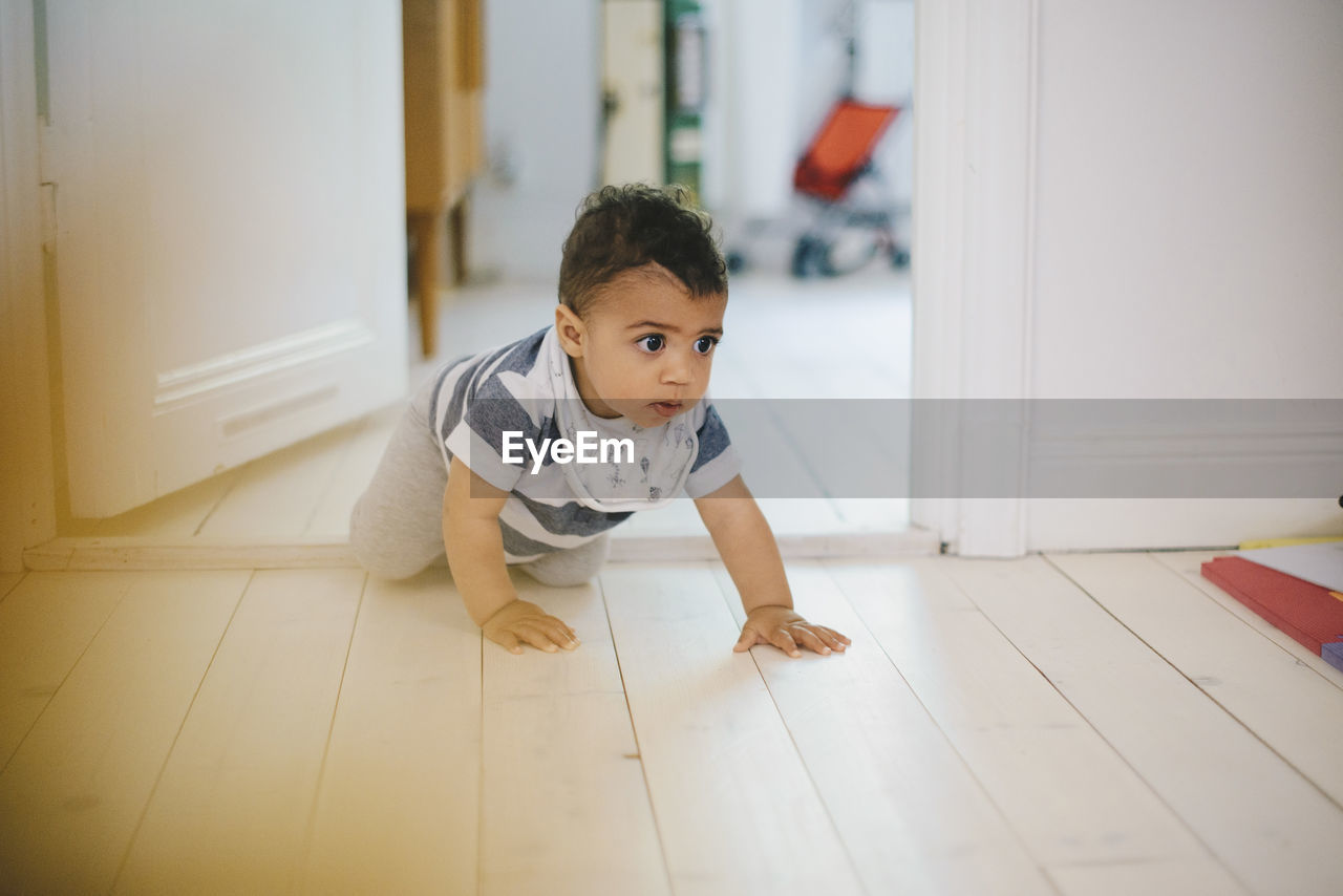 Toddler looking away while crawling on floor at home