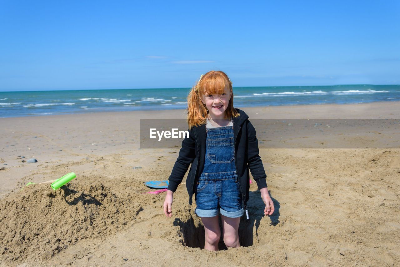 Happy girl standing on beach against sky
