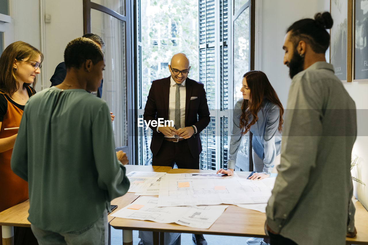 Businessmen and businesswomen discussing over blueprint on table in office