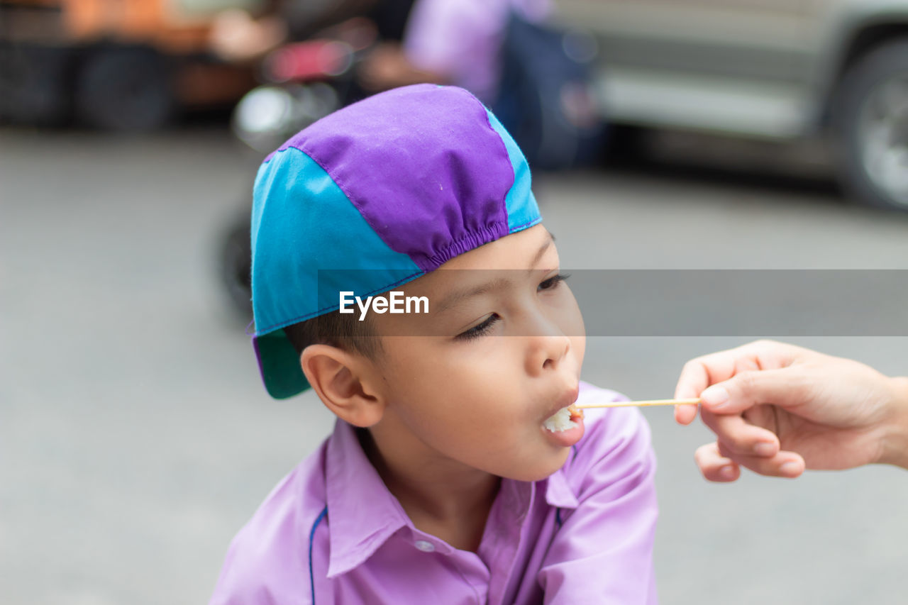 Cropped hand of mother feeding lollipop to son standing on road