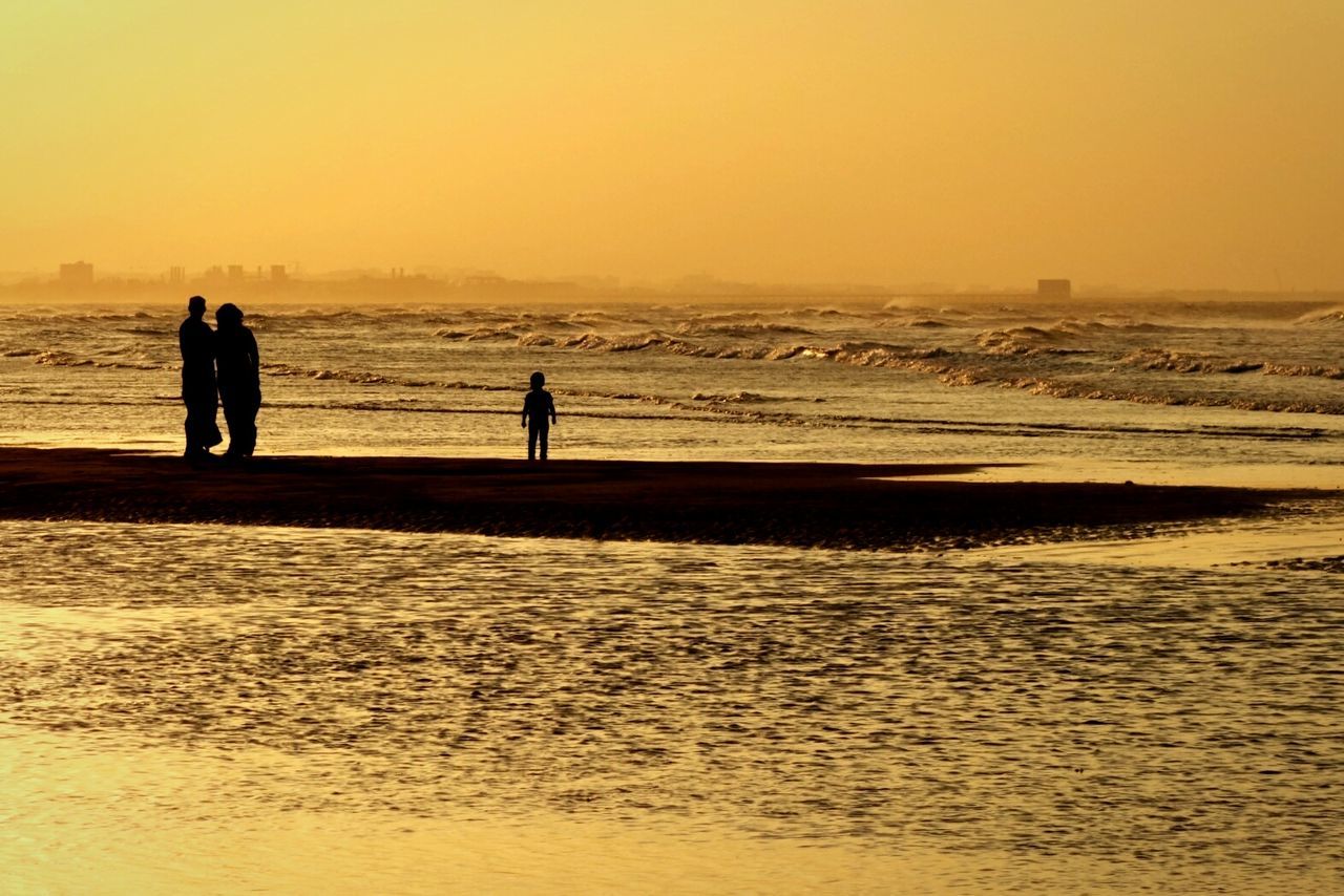 Silhouette people standing at sea shore during sunset