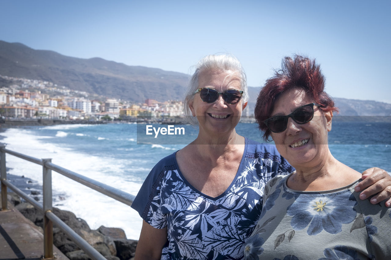 Portrait of smiling senior friends standing against sea