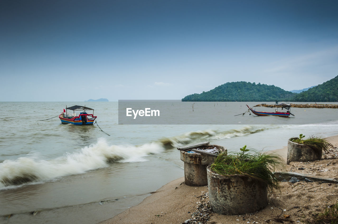 Mid distance view of fishing boats moored in sea against sky