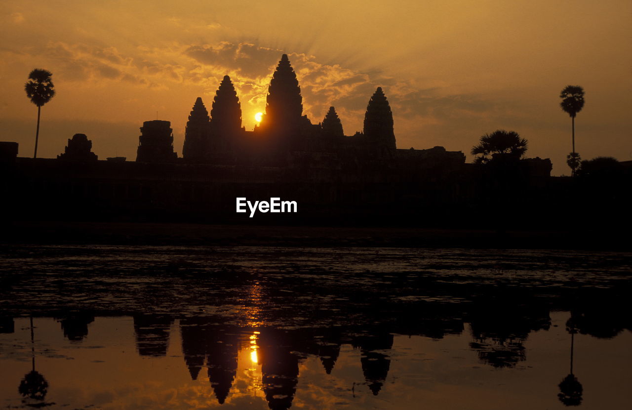 Silhouette temple reflecting in pond against sky during sunset