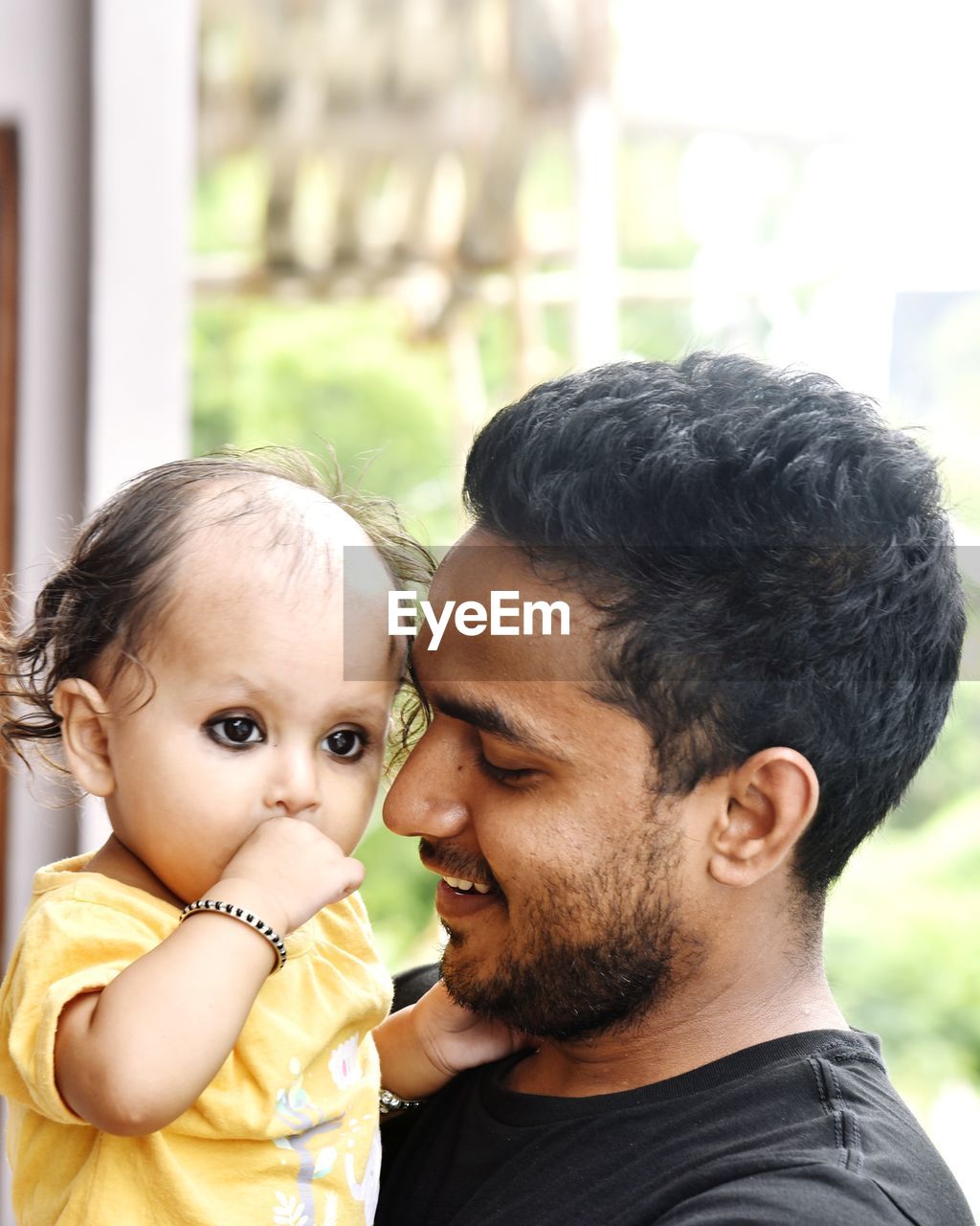 Side view of smiling father holding daughter by window at home