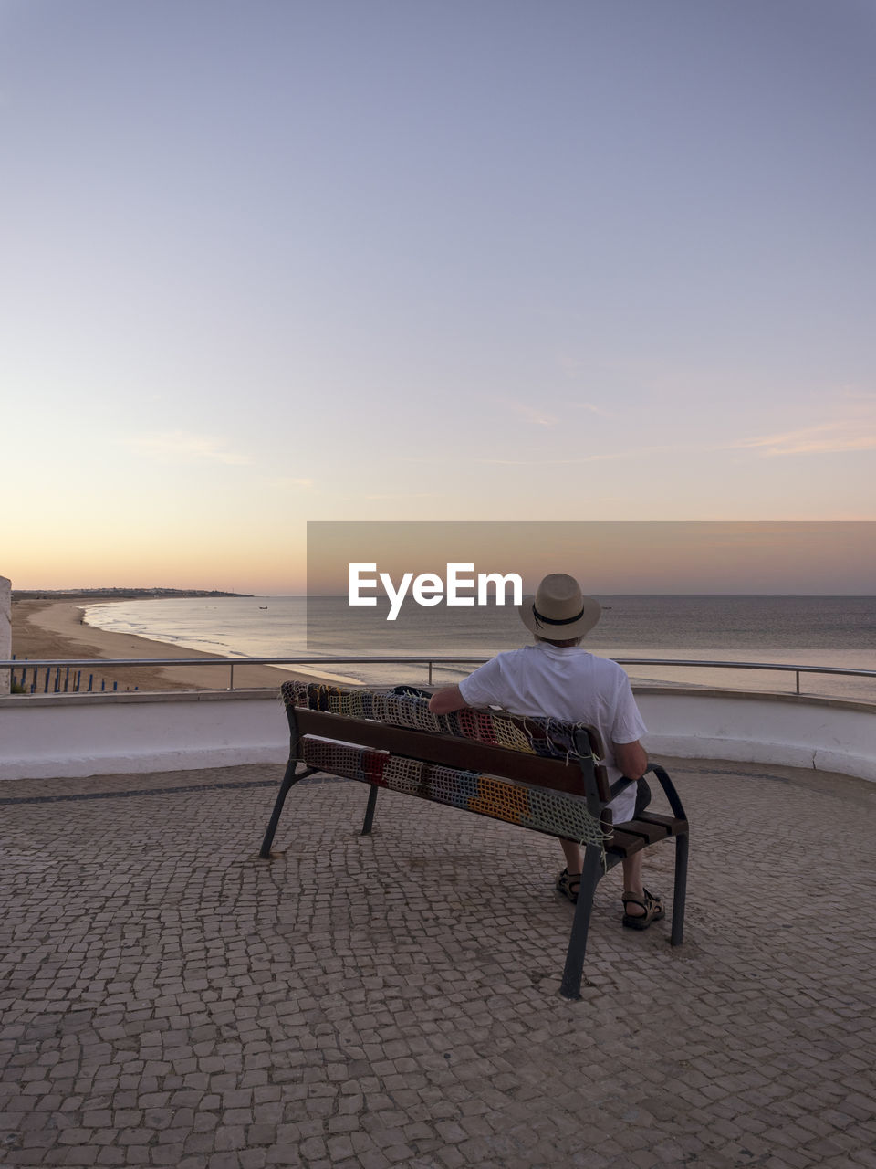 Portugal, senior man siting on bench watching sunrise