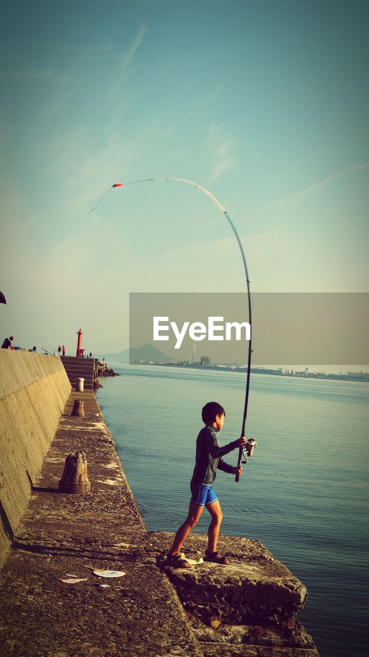 Side view of boy casting fishing line in sea