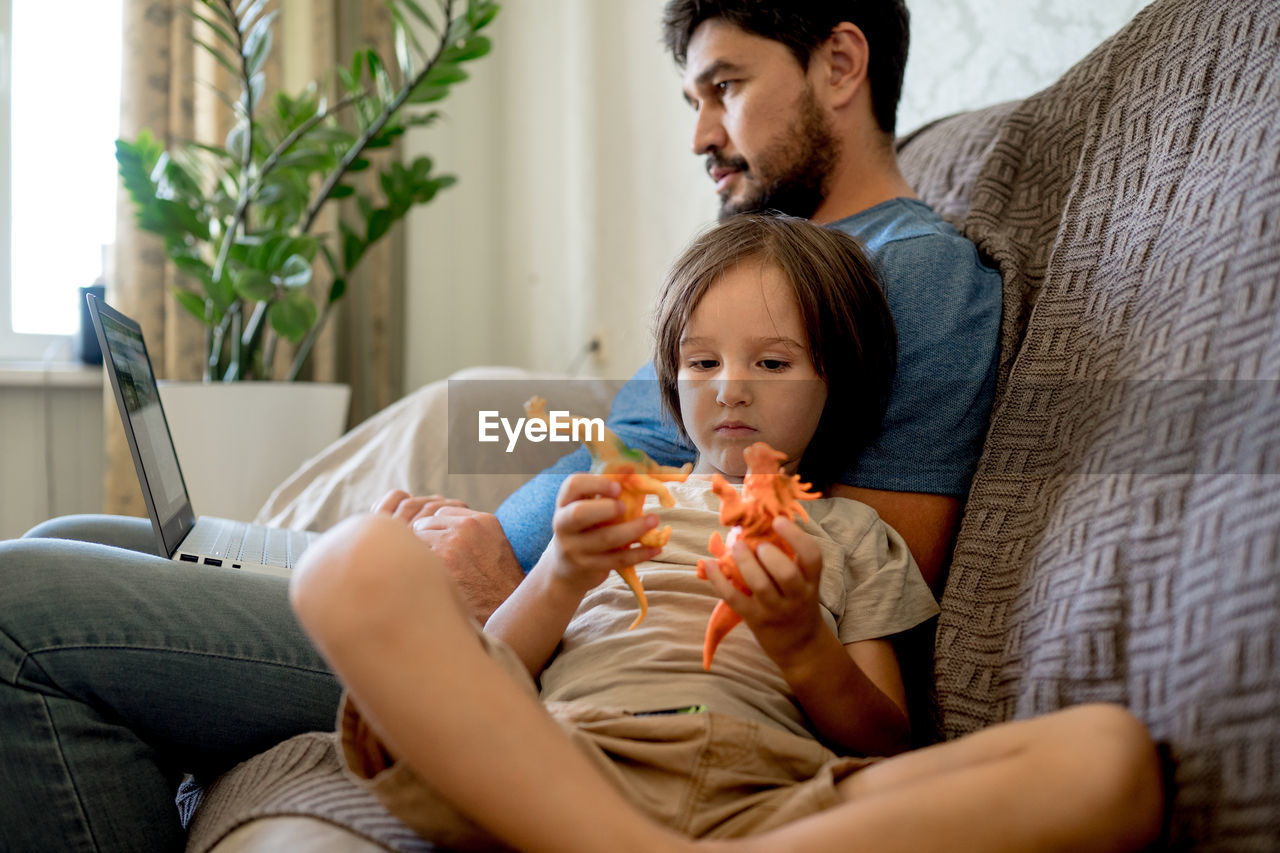 side view of young woman using mobile phone while lying on sofa at home