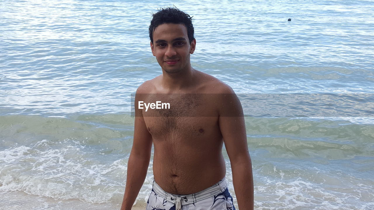 PORTRAIT OF YOUNG MAN STANDING ON BEACH