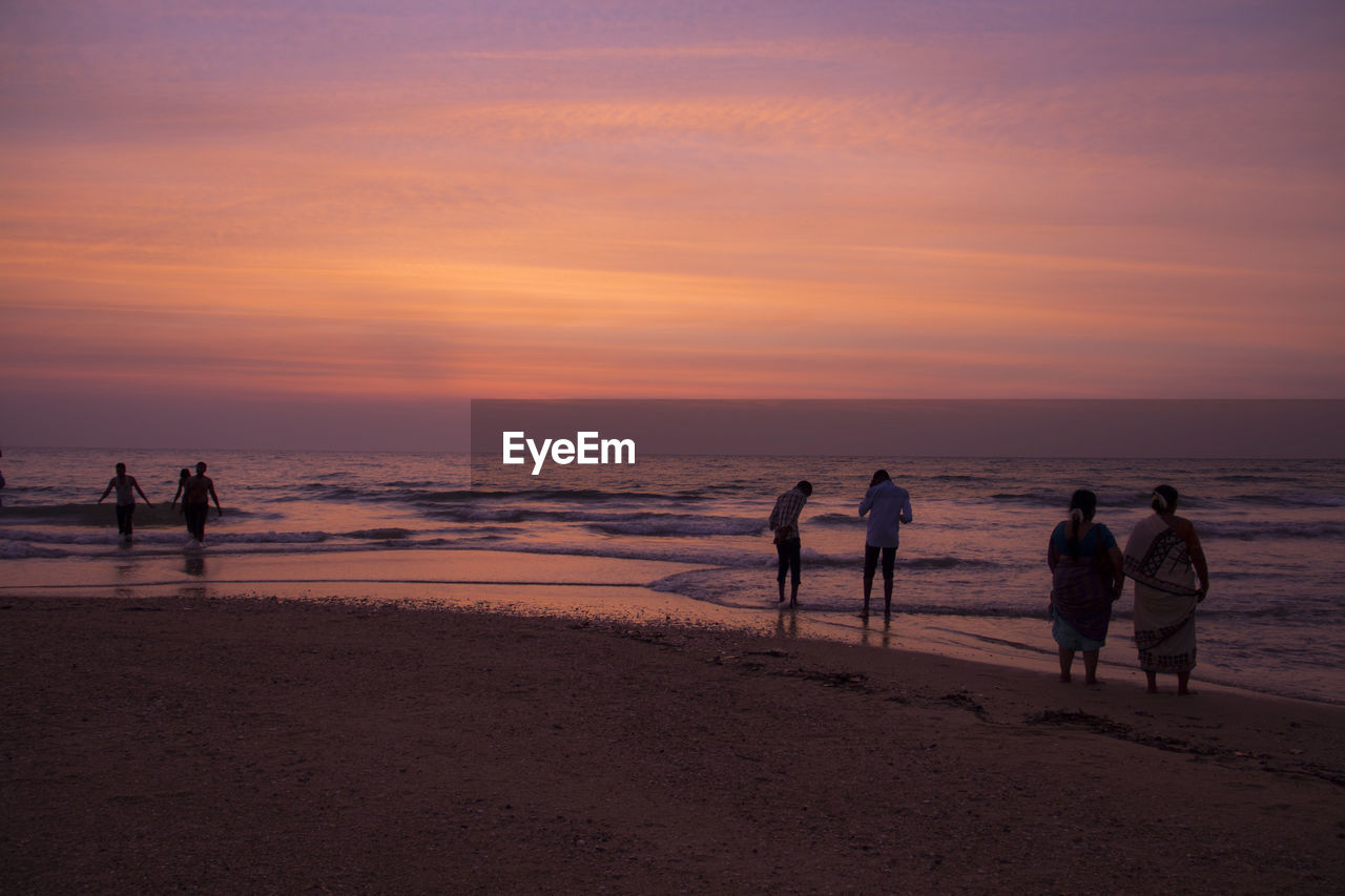 Silhouette people at beach against sky during sunset