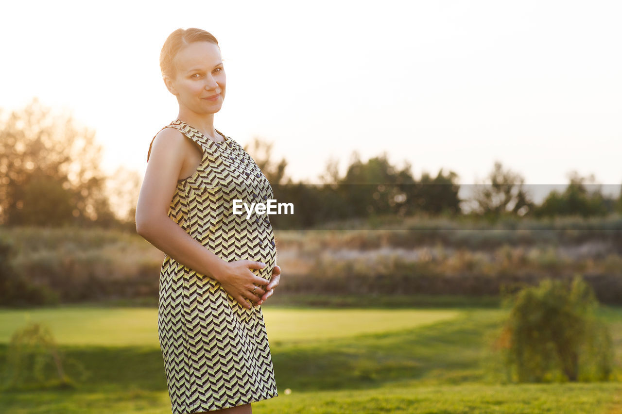 PORTRAIT OF A SMILING YOUNG WOMAN STANDING ON FIELD