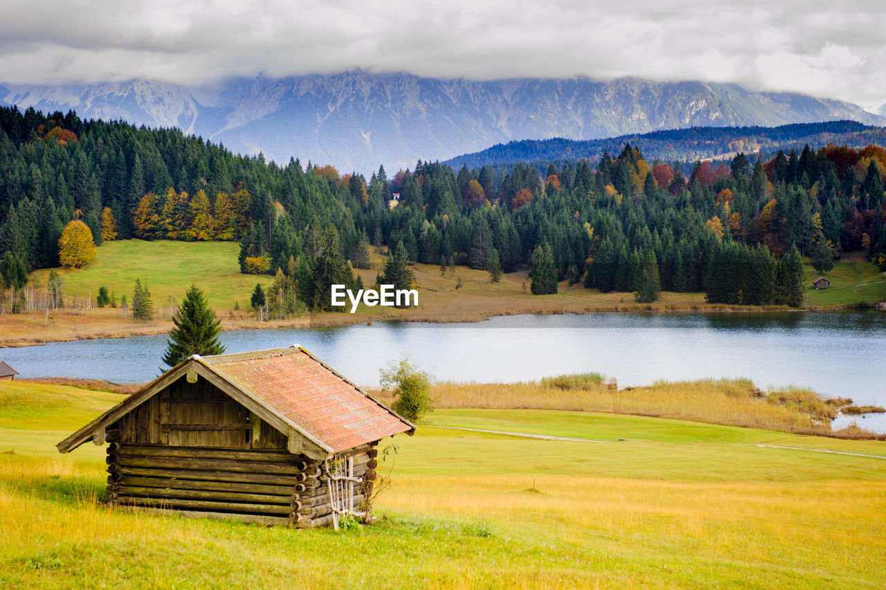 Hut on field by lake against mountains