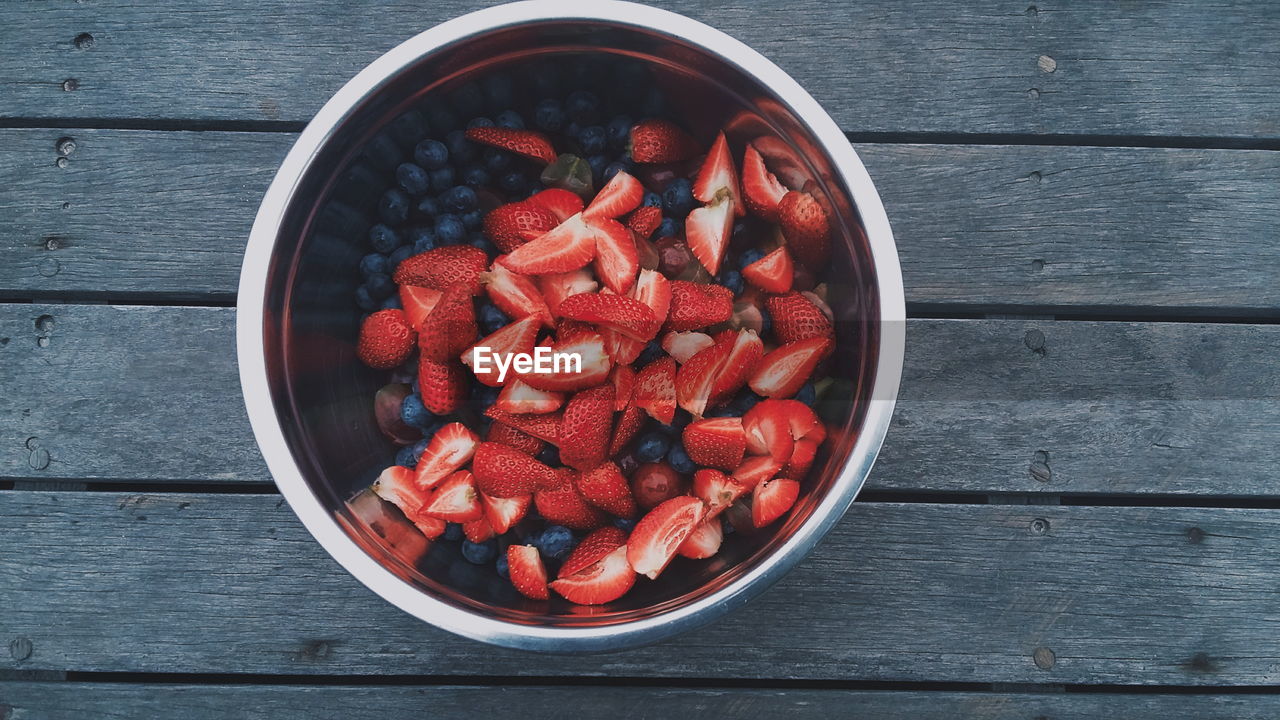 High angle view of berry fruits in bowl on wooden table