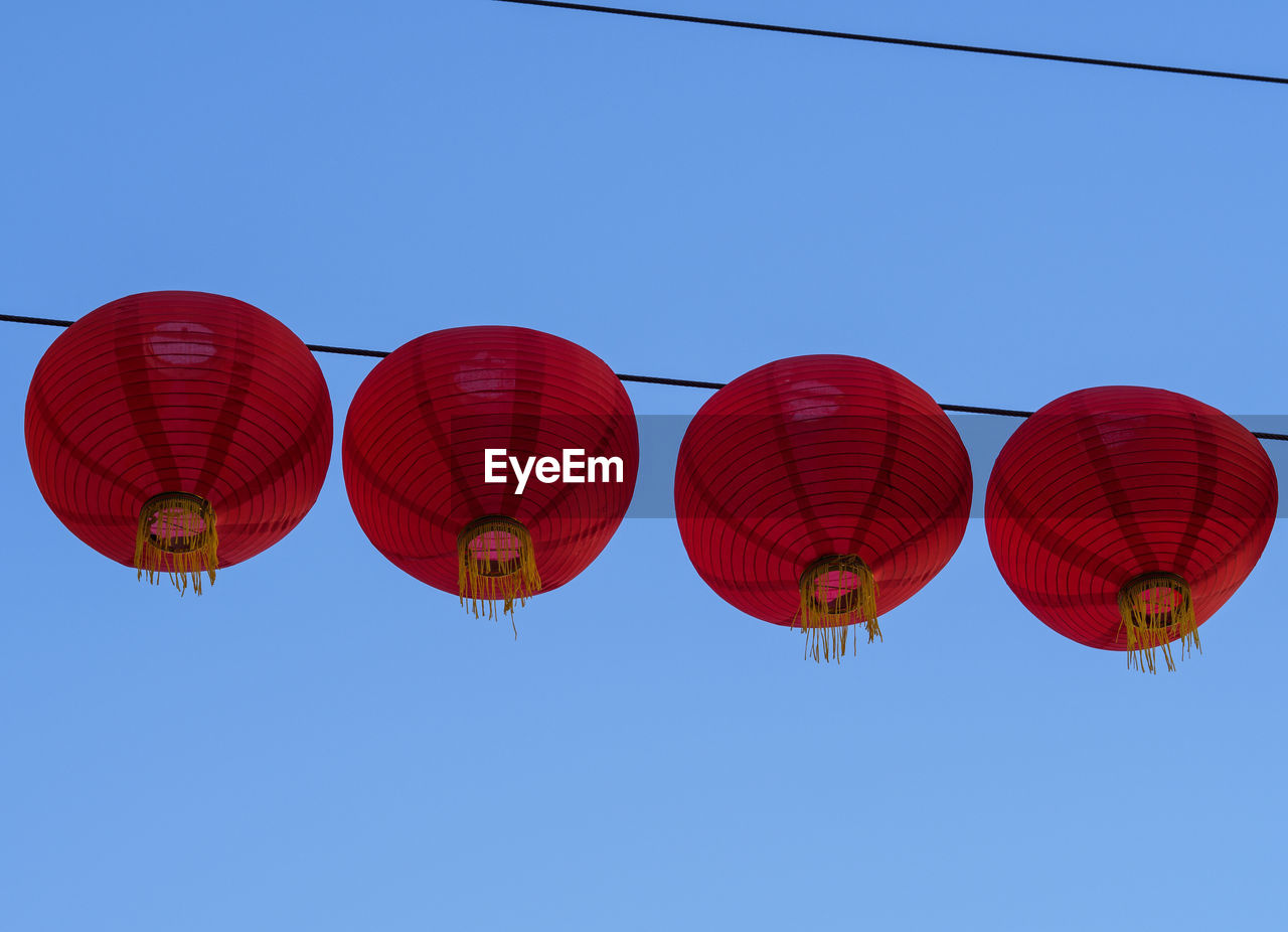 Low angle view of chinese lanterns hanging against clear blue sky