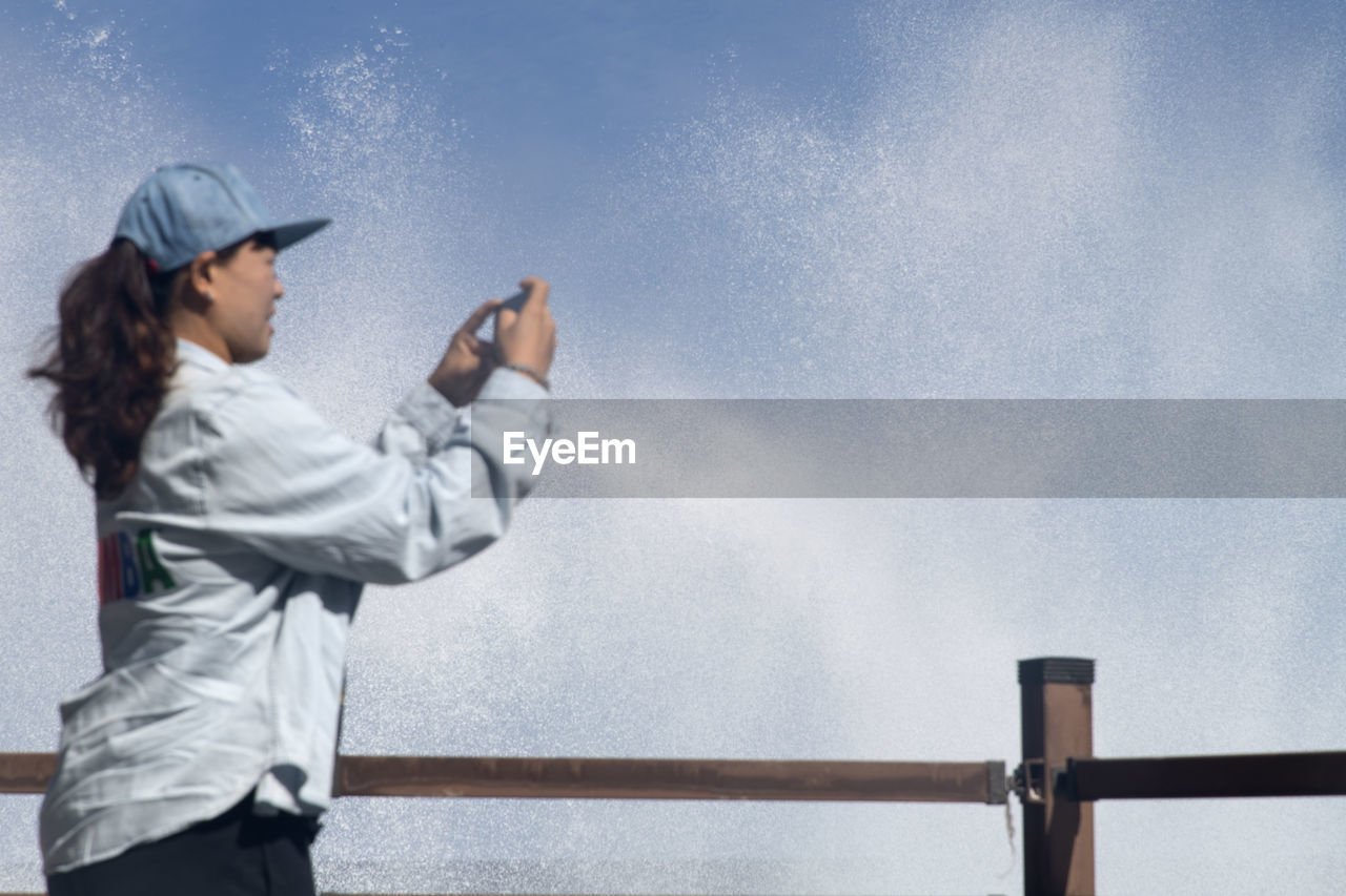 SIDE VIEW OF A WOMAN STANDING AGAINST SKY