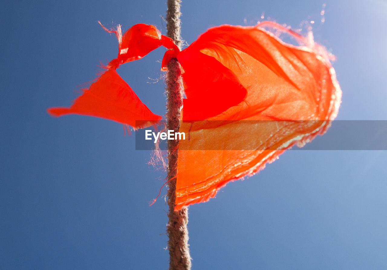 Low angle colour shot of a frayed piece of orange bunting tied to a rope against a clear blue sky