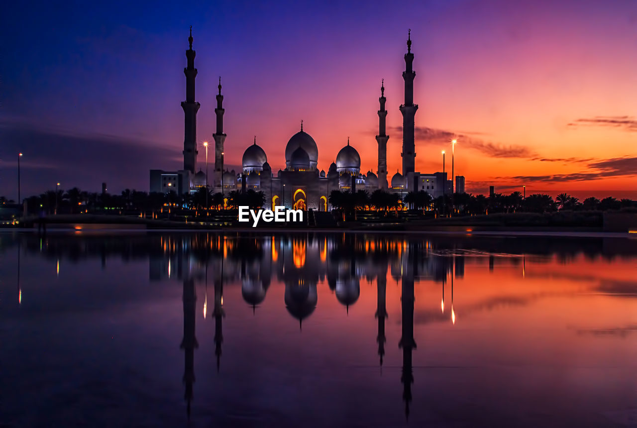 Reflection of illuminated mosque against sky during sunset