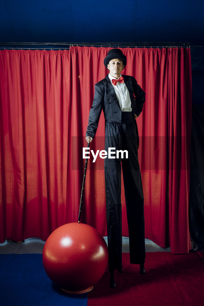 Male performer standing on stilts in front of red curtain