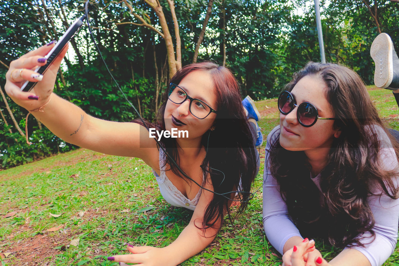 Female friends taking selfie while lying on grass at park