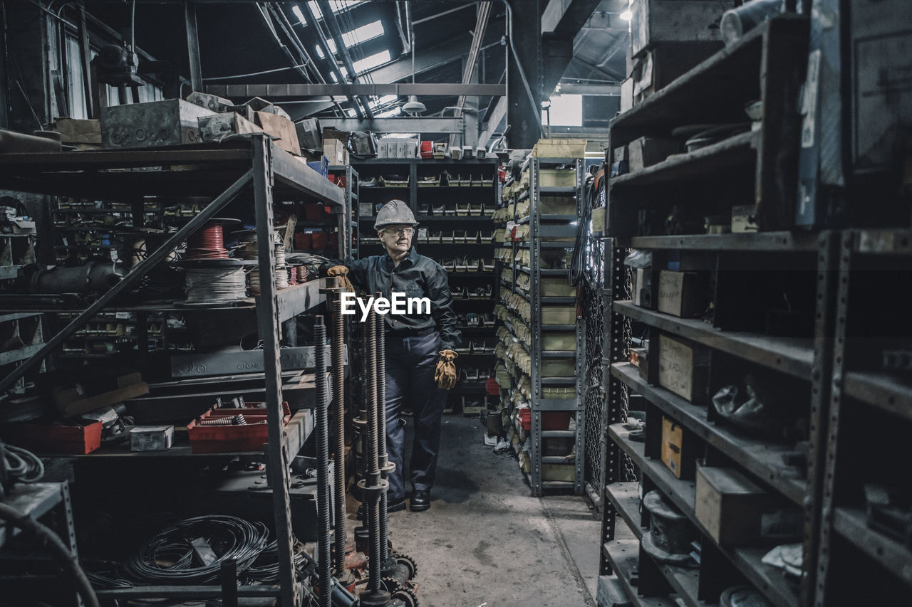 Female worker looking away while leaning on rack in factory