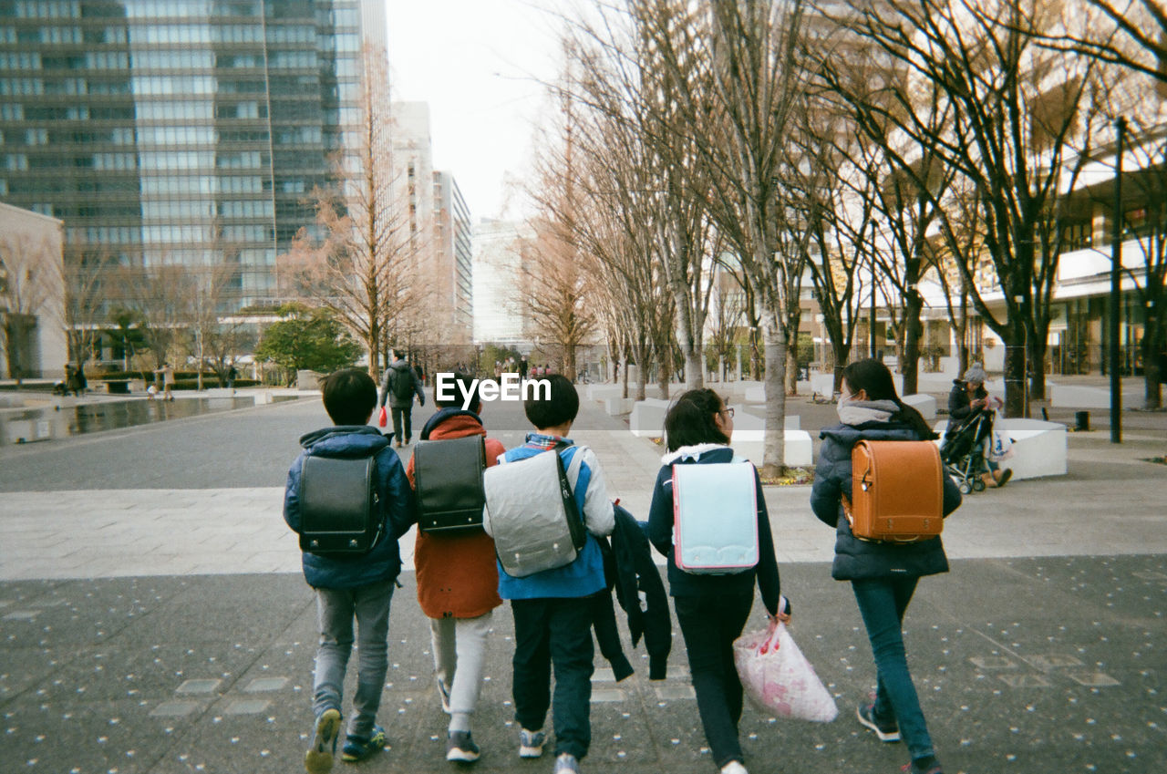 Rear view of backpack people walking on street in city