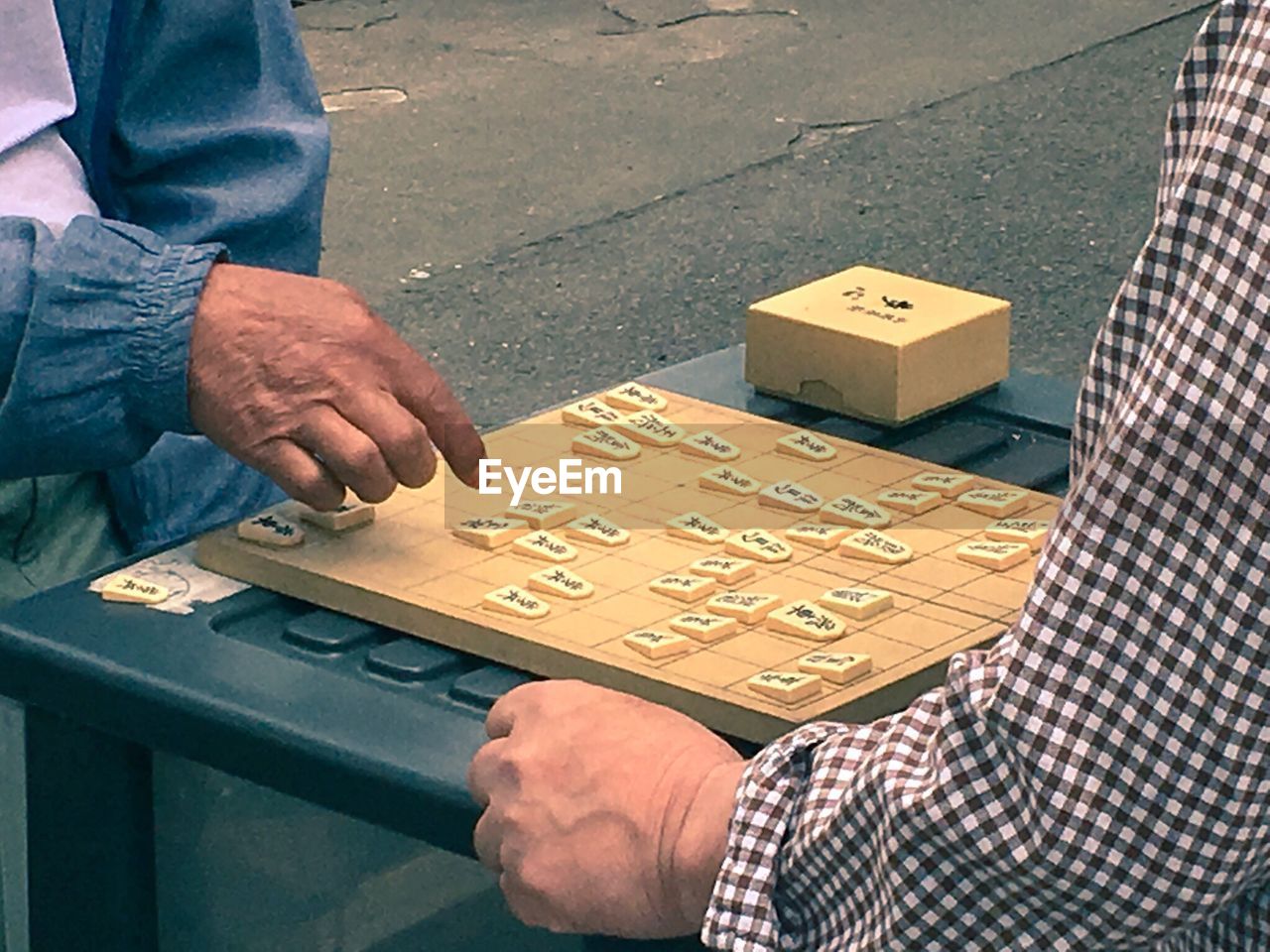 Midsection of male friends playing shogi while sitting outdoors